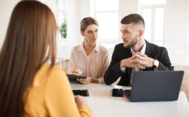 Tre personer diskuterar ett affärsupplägg vid ett bord med laptop